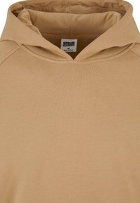 Beige hettegenser med vid halslinning, mykt stoff og en merkelapp som sier "Urban Classics." Har ribbede kanter og minimal detaljering.