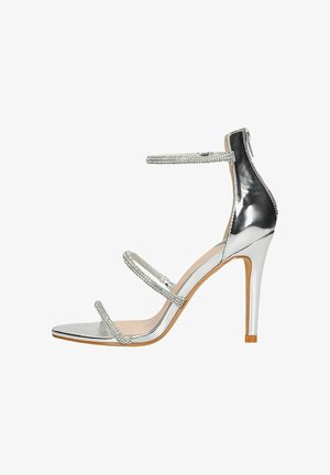 Sandalini argentati con tacco alto, tre cinturini arricchiti da strass, punta affusolata e una finitura a specchio elegante. Caratterizzati da un sottile tacco a stiletto.