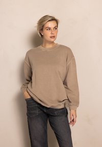Beige sweatshirt featuring a crew neck, drop shoulders, and ribbed cuffs. Paired with dark gray pants, the fabric appears soft with minimal texture.