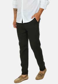 Pantaloni neri in lino con una vestibilità affusolata, caratterizzati da una texture liscia e orli arrotolati. Abbinati a una camicia bianca con bottoni e mocassini beige.