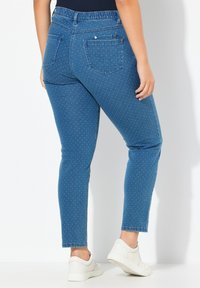 Jeans de mezclilla azul con un diseño ajustado, patrón de puntos y cintura elástica. Presentan dos bolsillos traseros y tobillos rematados. Llevados con zapatillas blancas.