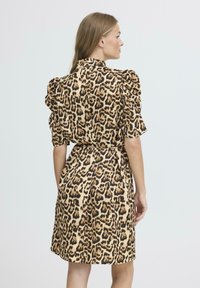 Robe imprimée léopard avec de courtes manches bouffantes, une taille ceinturée et une jupe fluide. Le matériau semble lisse avec une texture douce.