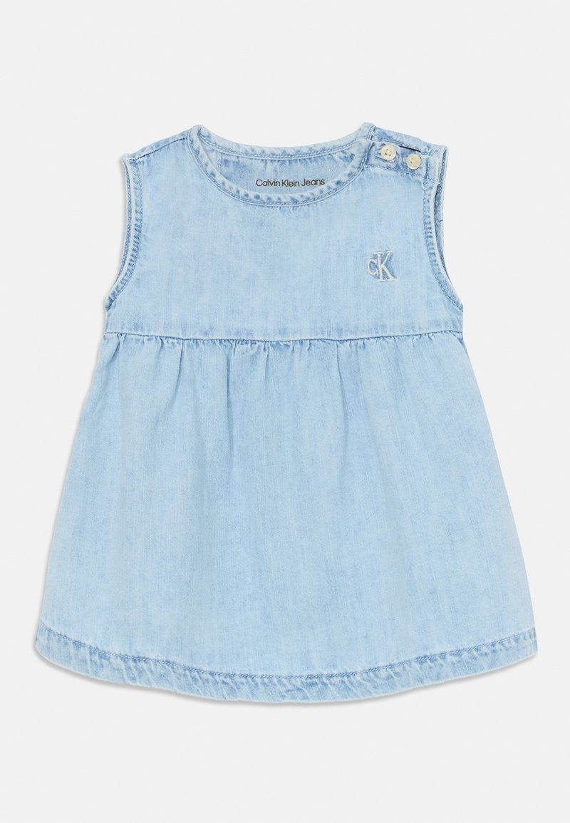 Vestido de mezclilla azul claro con diseño sin mangas, cintura fruncida y acentos de botón en los hombros. Presenta un logo bordado de "ck" en la parte frontal.