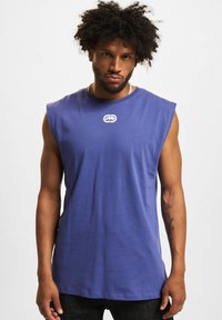 Blue sleeveless shirt made of cotton, featuring a round neckline and a small logo on the chest. Smooth texture and casual design.