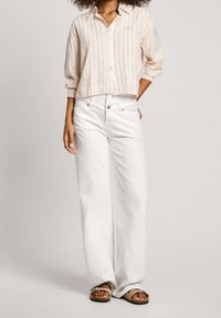 White wide-leg jeans paired with a cropped, striped button-up shirt in pastel orange and cream. Sandals with a strap detail visible.