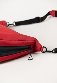 Rote Slingtasche aus wasserdichtem Stoff, mit einer Reißverschlusstasche, verstellbarem schwarzen Träger und strapazierfähigem schwarzen Zubehör.