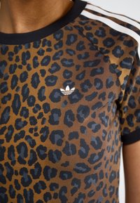 Camiseta de jersey con estampado de leopardo en marrón y negro, con cuello redondo, ribete negro y mangas a rayas blancas. Presenta un pequeño logo en el pecho.