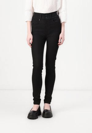 Black skinny jeans with a high waist, two-button closure, front pockets, and a smooth fabric texture. Worn with black platform shoes.