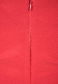 Vêtement rouge à fermeture éclair avec texture côtelée. Une fermeture éclair centrale court verticalement dans le dos, avec des coutures nettes le long des bords.