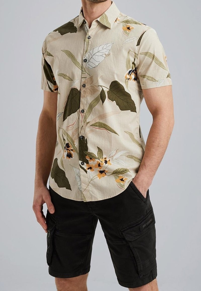 Kortærmet, beige blomstrede skjorte med knapper og grønne og orange bladmønstre; parret med sorte cargo shorts med sidelommer.