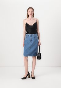 Camisola di raso nera, gonna a tubino in denim a vita alta, texture liscia, colore azzurro chiaro, scarpe nere con tacco alto, piccola borsa nera.