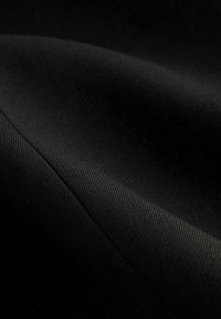 Gros plan d'un tissu noir montrant une couture diagonale et une texture tissée fine avec des plis doux et des ombres légères.