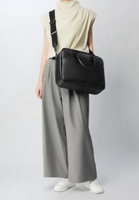 Bolso de piel negra con asas dobles y una correa de hombro ajustable. Forma rectangular y textura suave, con detalles de diseño minimalistas.