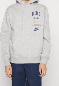 Grå sweatshirt med huva, med flera Nike-logotyper i olika färger. Tillverkad av mjukt material med en framficka och ribbad muddar.