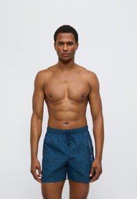 Αντρικό μαγιό βερμούδα σε βαθύ τιρκουάζ με σχέδιο φύλλων. Διαθέτει ελαστική μέση και κορδόνι για ρύθμιση.