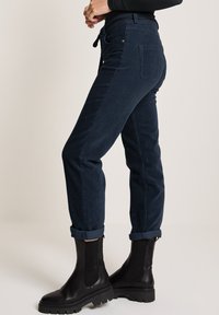 Marina kordflanellbyxor med avsmalnande ben och uppvikta fållar, med en knytdetalj framtill och sidofickor, i kombination med svarta ankelboots.