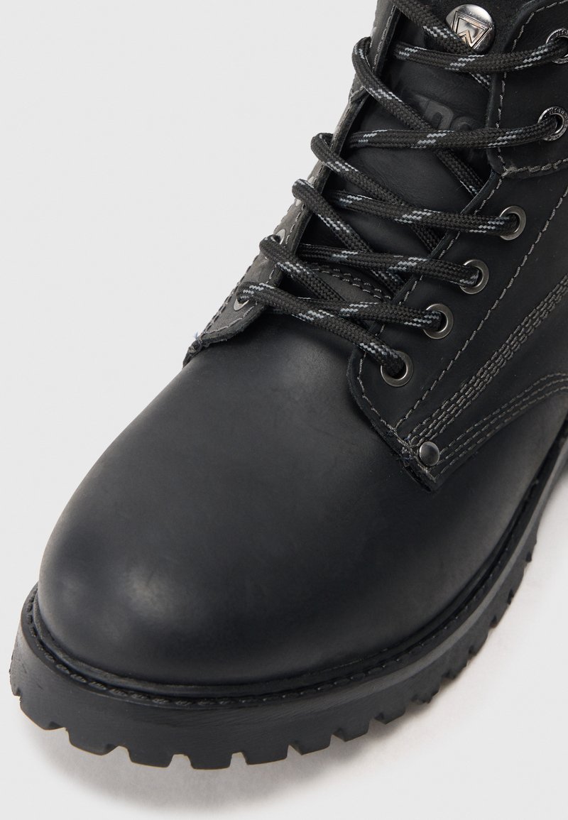 Bota de cuero negra con punta redondeada, superficie texturizada, cordones grises y suela resistente con profundas protuberancias para mayor tracción.