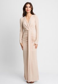 Długa, dopasowana sukienka z połyskującego beżowego materiału. Charakteryzuje się głębokim dekoltem w kształcie litery V, długimi rękawami i marszczeniami w talii. Gładka struktura.