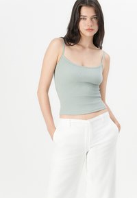 Λαμπερό πράσινο ριγωτό τοπ με λεπτές τιράντες, συνδυασμένο με χαλαρές λευκές λινές παντελόνες που διαθέτουν ελαστική μέση και τσέπες.