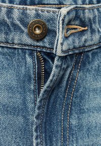 Jeans de mezclilla azul abotonados con cremallera, que cuentan con herrajes de metal cepillado y costuras doradas en contraste a lo largo de las costuras.