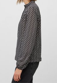 Blusa stampata in bianco e nero con scollatura tonda, maniche lunghe con polsini elasticizzati e vestibilità larga. Il motivo include piccole forme floreali.