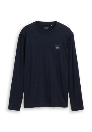 T-shirt à manches longues bleu marine en coton. Il présente un col rond et une petite étiquette logo sur le côté gauche de la poitrine avec un texte jaune.