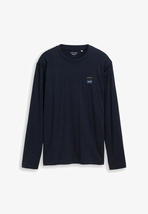 T-shirt à manches longues bleu marine en coton. Il présente un col rond et une petite étiquette logo sur le côté gauche de la poitrine avec un texte jaune.
