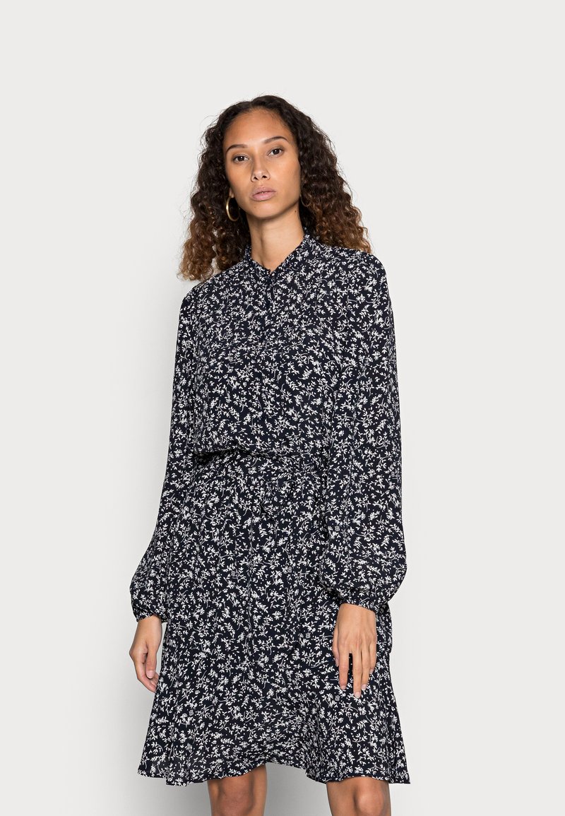Abito blu navy con motivo floreale bianco, maniche lunghe, colletto abbottonato e gonna svasata, realizzato in tessuto leggero.