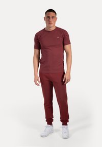 Conjunto deportivo burdeos que incluye una camiseta de manga corta y joggers, confeccionado en una tela suave. Joggers ajustados con puños, combinados con zapatillas blancas.
