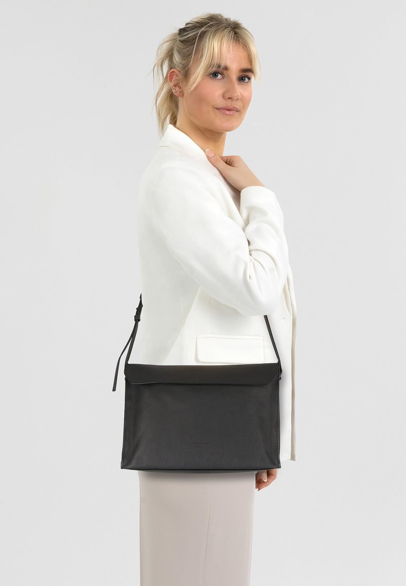 Czarna skórzana torba na ramię o teksturowanym wykończeniu, z suwakiem i regulowanym paskiem. Prosty design, prostokątny kształt, bez widocznych elementów metalowych.