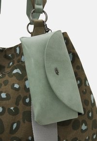 Portafoglio verde in suede con un fermaglio in metallo attaccato a una tracolla di stoffa con motivo mimetico, dotata di anelli metallici.