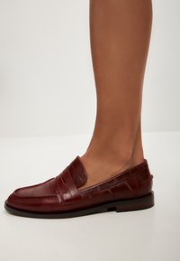 Burgunderfarbene Leder-Loafers mit horizontalen Riemen, mandelförmigem Zehendesign, glatter Textur und niedrigem, gestapeltem Absatz.