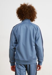 Chaqueta deportiva azul con un alto cuello, textura acolchada y franjas laterales en contraste en navy. Incluye puños y dobladillo acanalados.