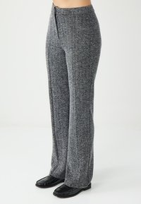 Pantalons larges à motif gris avec une finition texturée, dotés d'une taille à cordon et d'une coupe décontractée, associés à des mocassins noirs.