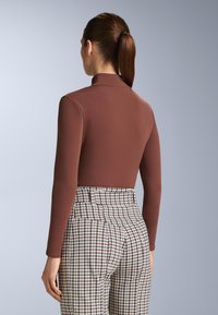 Brun långärmad bodysuit med hög krage, kombinerad med svartvita högmidjade byxor i hundtandsmönster. Slät textur, åtsittande design.