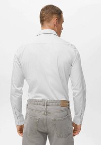 Witte lange mouwen shirt met enkele knoopmanchetten, getailleerde pasvorm en een rugplooi, gecombineerd met lichtgrijze spijkerbroek met een leren patch.