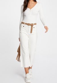 Bílý top s dlouhým rukávem, výstřihem do V a kroužkovým zipem, doplněný bílými širokými džíny s hnědým pásem a teniskami. Součástí je i kabelka s třásněmi.