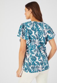 Camiseta de manga corta con estampado de hojas en tonos verde azulado y blanco, fabricada en un tejido suave, con corte relajado y detalles de volantes en los hombros.
