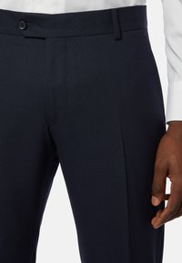 Námořnické společenské kalhoty z texturované látky, s plochým předním dílem, s jedním knoflíkem a bočními kapsami; vyznačují se přiléhavým střihem a záhybem podél nohy.