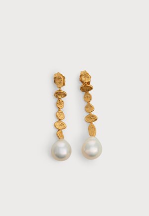 Boucles d’oreilles goutte en or avec des maillons texturés irréguliers et de grands pendentifs en perles blanches sur un fond clair uni.