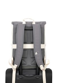 Backpack in gray fabric with padded straps, textured surface, and integrated handle. Attached to a black suitcase with a retractable handle.