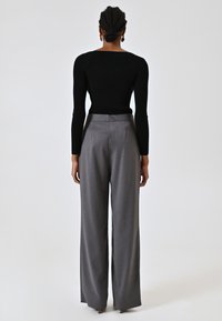 Zwarte ribgebreide longsleeve top gecombineerd met hooggesneden, wijde grijze broek met een gladde afwerking. Geen zichtbare patronen of hardware-details.