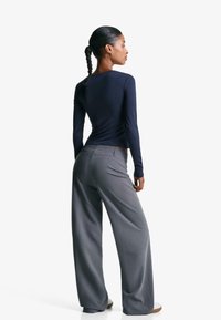 Marinblå långärmad topp och grå vida byxor. Toppen har en figursydd design; byxorna har en slät, skräddarsydd look med fickor.