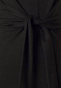 Černá šatová látka s uzlovým detailem v pase, hladkou texturou a přiléhavým střihem, který zdůrazňuje siluetu.