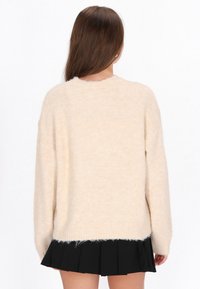 Beige tröja med mjuk, luddig textur, rund halsringning och sänkta axlar, kombinerad med en svart plisserad kjol.