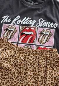 Hallidehall t-särk, millel on The Rolling Stonesi logo ja värvilised keeled; koos leopardimustriliste lühikeste pükstega, millel on elastne vöökoht.