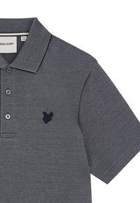 Grå polo skjorte i et struktureret stof med en kontrasterende krave. Har tre knapper og et marineblåt sommerfugllogo på brystet.