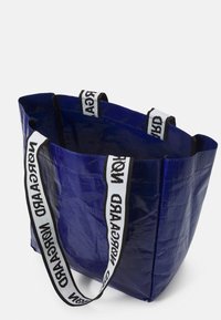 Sac fourre-tout bleu en matériau brillant, doté de sangles à motifs noir et blanc. Ouvert sur le dessus avec une conception spacieuse et des côtés droits.