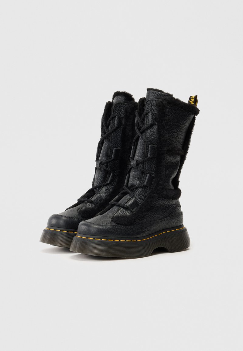 Bottes noires avec une tige en cuir texturé, des accents en fourrure le long de la tige, des lacets et une semelle épaisse avec des coutures jaunes.