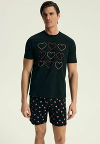 Czarna koszulka z wzorem serc w czerwonym konturze, zestawiona z czarnymi szortami z małymi, wielokolorowymi wzorami serc. Miękki materiał, codzienny krój.